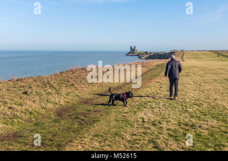 Ein Mann, der seinen Hund an Reculver Towers, Reculver, Kent, Großbritannien entlang der Klippe Spaziergang an der Küste in der Nähe von Herne Bay und Whitstable. Stockfoto