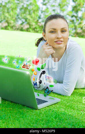 Junge Mädchen, die auf dem Gras mit ihren Laptop. Artwork Stockfoto