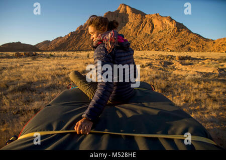 Frau sitzt auf der Crash Pad auf 4x4 Auto Dach feste während Bouldern Expedition, Spitzkoppe, Erongo Region, Namibia Stockfoto