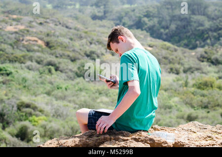 Teenaged Jungen sein Smartphone prüfen, während auf einem Felsen in Torrey Pines State Preserve in La Jolla, Ca, USA. Stockfoto