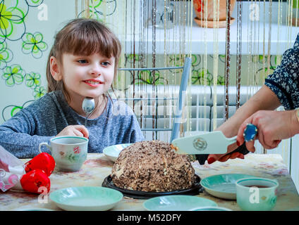 Kleines Mädchen schaut mit Interesse, wie die Mutter ihre Schichten ein Stück leckeren Kuchen. Stockfoto