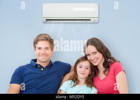 Glückliche Familie sitzt auf dem Sofa unter der Klimaanlage zu Hause Stockfoto