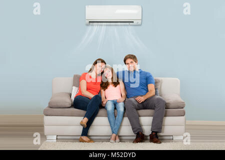 Glückliche Familie sitzt auf dem Sofa unter der Klimaanlage zu Hause Stockfoto