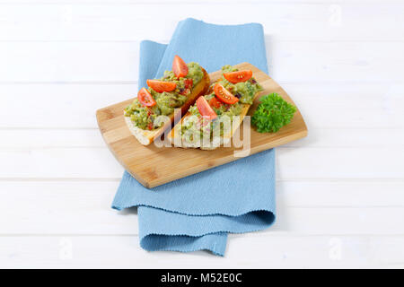 Frisches Baguette mit Guacamole und Tomaten auf Holz Schneidebrett Stockfoto