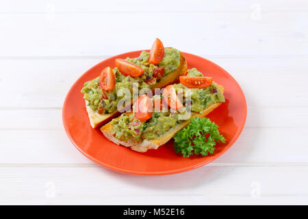 Frisches Baguette mit Guacamole und Tomaten auf rote Platte Stockfoto