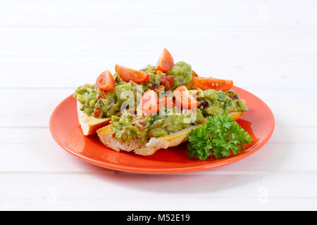 Frisches Baguette mit Guacamole und Tomaten auf rote Platte Stockfoto