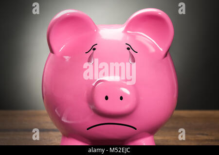 Nahaufnahme eines traurigen rosa Sparschwein gegen grauer Hintergrund Stockfoto