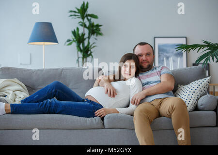 Fotos von glücklichen schwangeren Frau und Mann auf graue Sofa Stockfoto