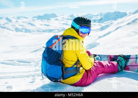 Bild von der Rückseite der Frau in Helm mit Rucksack auf Schnee mit Snowboard Stockfoto