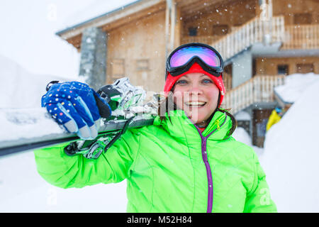 Frau in Helm mit Skier auf die Schulter auf dem Hintergrund der Gebäude aus Holz Stockfoto