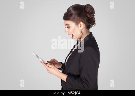 Profil Seite Geschäftsfrau, Tablet, offenen Mund, schockiert. Studio shot, Indoor. Auf grauem Hintergrund Stockfoto