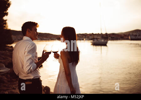 Romantisches Paar trinken Wein bei Sonnenuntergang an einer Pier auf einem Meer. Romanze. Zwei Menschen, die sich einen romantischen Abend bei einem Glas Wein in der Nähe des Meeres. Stockfoto