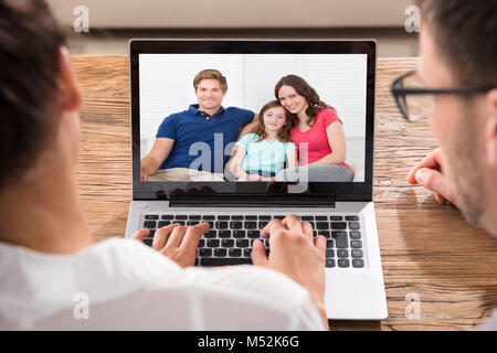 Close-up von zwei Menschen Videokonferenzen mit Familie auf Laptop am Schreibtisch Stockfoto