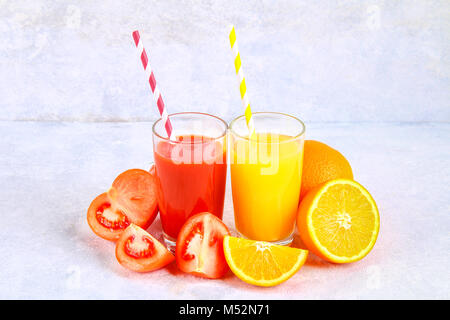 Gläser mit Orangensaft, Tomatensaft mit farbigen Tubuli auf grauem Beton Tabelle. Scheiben von Obst und Gemüse um Stockfoto