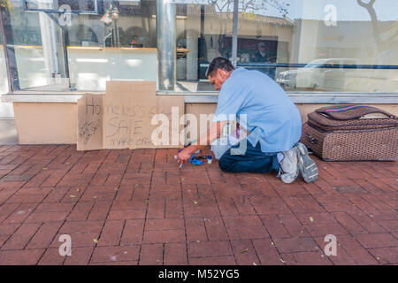 Eine Obdachlose erwachsenen männlichen stellt einen Ramschverkauf vor einem freien Store Front auf der State Street. Er hat einen Karton mit Handschrift auf Es announcin Stockfoto