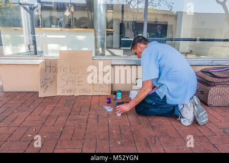 Eine Obdachlose erwachsenen männlichen stellt einen Ramschverkauf vor einem freien Store Front auf der State Street. Er hat einen Karton mit Handschrift auf Es announcin Stockfoto