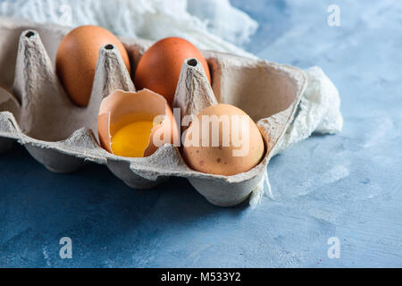 Frische Eier, ganze und gebrochen, in einem Papier Verpackung auf einen konkreten Hintergrund. Frische Zutaten für Ostern kochen. Close-up mit Kopie Raum Stockfoto