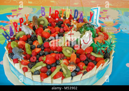 Ein erster Geburtstag Kuchen mit Sommer Obst, Spielzeug Tiere und Geburtstag Kerzen dekoriert. Stockfoto