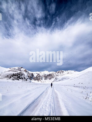 Person Weg hinunter eine verschneite Straße durch Feld Land in einer malerischen Landschaft konzeptuelle der Jahreszeiten. Stockfoto