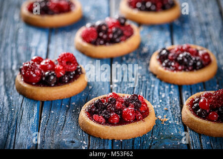 Leckere Törtchen mit Beeren auf Blau Holz- Hintergrund Stockfoto