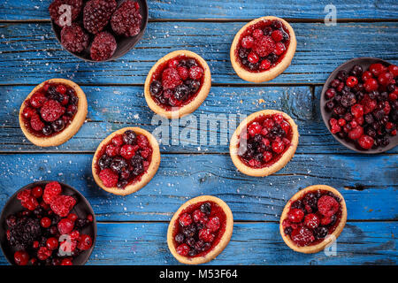 Köstlichen Beerenfrüchten mini Torten (Törtchen) auf blauem Hintergrund Holz Stockfoto