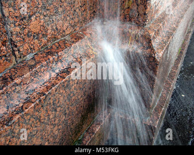 Ein starker Strahl Wasser aus dem abflußrohr auf der granitmauer während der regensturm Stockfoto