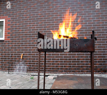 Brennholz und Brand im alten rostigen Holzkohlegrill auf Mauer Hintergrund Stockfoto