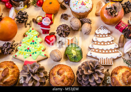 Früchte, Weihnachtsplätzchen, ein Spielzeug Weihnachtsmann, Muttern, Tannenzapfen mit Schokolade Bonbons auf ein Plywood Table Stockfoto