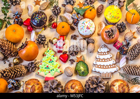 Weihnachtsplätzchen, Früchte, ein Spielzeug Weihnachtsmann, Muttern, Tannenzapfen mit Schokolade Bonbons auf ein Plywood Table Stockfoto