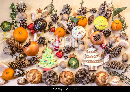 Weihnachtsplätzchen, Spielzeug, Santa Claus, Früchte, Nüsse, Tannenzapfen mit Schokolade Bonbons auf ein Plywood Table Stockfoto