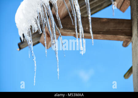 Eiszapfen und Schnee überhängenden Dach. Reihe langer und großen Eiszapfen auf dem Dach in den Schnee. Stockfoto