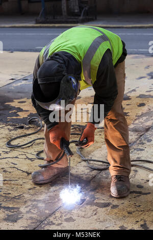 Ein Arbeiter Schweißen eine Stahlplatte auf einem New York City street. Stockfoto