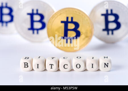 Einzelnes Wort BITCOIN aus Holzklötzen mit mehreren goldenen und silbernen Bitcoin Münzen stehen auf weißen Hintergrund, cryptocurrency Konzept Stockfoto