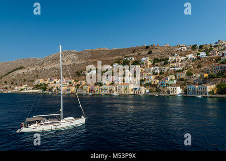 Eine Yacht nähert, (oder Symi Symi), eine kleine Insel der Dodekanes, Griechenland, dass die Besucher mit der ruhigen Atmosphäre und die herrliche Architektur überrascht Stockfoto