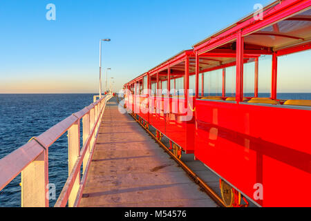 Perspektivische Ansicht von Vintage red elektrische Zug am Jetty Busselton Titel in Busselton, Western Australia. Berühmte Ort bei Sonnenuntergang. Busselton Jetty ist die längste hölzerne Seebrücke in der Welt. Stockfoto