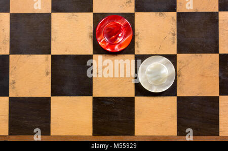 Zwei runde rote und weiße perlmuttfarbene Stücke auf einem alten Holz- Schachbrett Stockfoto