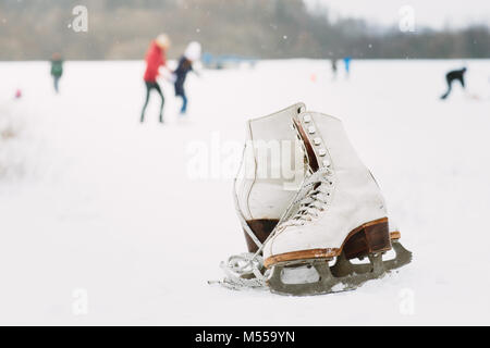 Ein paar weibliche Schlittschuhe liegen auf dem Schnee mit Skater im Hintergrund Stockfoto