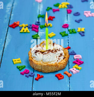 Süße Kuchen mit weißer Creme und eine brennende Kerze gelb auf blauem Hintergrund Holz, Happy Birthday Inschrift Stockfoto