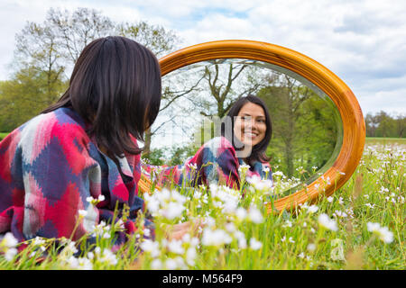 Liegende Frau mit Spiegel in der blühenden Wiese Stockfoto