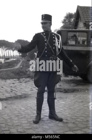 1920s, historische Bild, ein junger französischer Polizist oder Gendarm" in seiner dekorativen Uniform, mit Tunika und Hose, stehend auf einem Dorf gepflasterten Straße mit Handzeichen zu direkten Kraftfahrzeuge der Ära. Die "Gendarmerie Nationale ist Teil der französischen Streitkräfte und hat seit dem Jahr 1791. Stockfoto