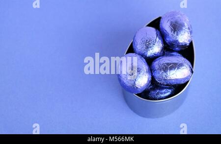 Ostern Karte mit violetten Farben, glänzend verpackt Schokolade Eier in einem Metall backen Form. Ostern Karte mit traditionellen Leckerbissen und Text Raum Stockfoto