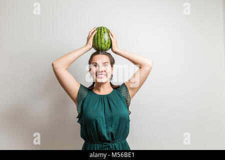 Lachend kaukasische Mädchen steht auf einem weißen Hintergrund mit Wassermelone auf dem Kopf isoliert Stockfoto