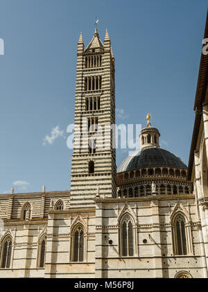 Fassade der Kathedrale von Siena mit Kuppel neben dem schwarz-weiß gestreiften Glockenturm Stockfoto