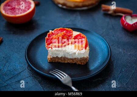 Mit Stück gebackene Käsetorte mit roten Pampelmuse Scheiben und vintage Gabel auf den schwarzen Stein Hintergrund mit Zutaten. Selektiver Fokus, Platz für Text. Stockfoto