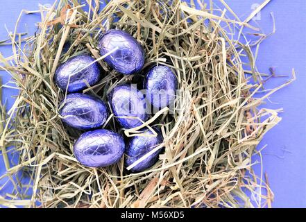 Eine Reihe von glänzenden Ostern Schokolade Eier, in Lila farbige Folie umwickelt. Kreative Ostern Konzept mit einem Nest aus Heu. Ansicht von oben Stockfoto