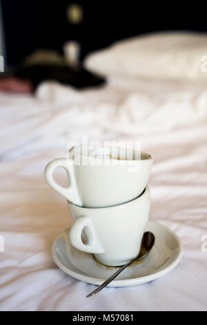 Zwei weiße Keramik leere Tassen Kaffee auf dem weißen Blatt ungemachten Bett Stockfoto