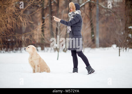 Bild von Mädchen in schwarzen Jacke training Hund in Snowy Park Stockfoto