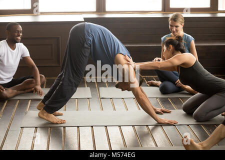 Weibliche Kursleiter helfen männliche Kursteilnehmer mit den nach unten schauenden Hund. Stockfoto