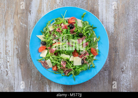 Frischer Salat - lecker frischer Salat mit Tomaten, Salat, Aubergine, Zucchini, Käse, Parmaschinken und Olivenöl, blauen Platte, grau Holz- Hintergrund Stockfoto