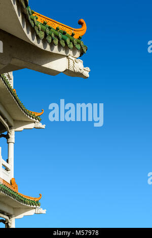 Chinesisch inspirierte geschwungenen Dach auf ein zeitgenössisches Gebäude mit dekorativen glasierten Dachziegeln und Dragon geformte konkreten Balken gegen den tiefblauen Himmel. Stockfoto